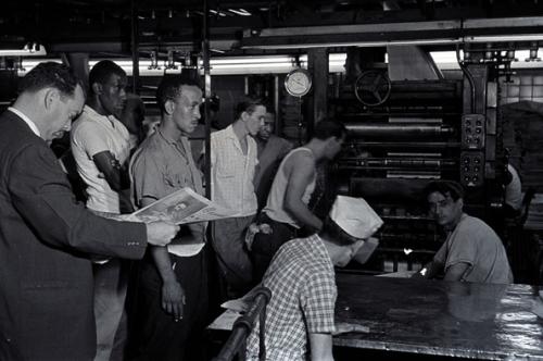 A la izquierda el primer director de Granma, Isidoro Malmierca, revisa el primer número del diario rodeado de un grupo de trabajadores. 